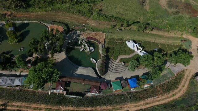 Aerial Da Lat Swan Sculpture Terraces, Curving Stone Steps And Reflective Ponds With White Swan Installation, Colorful Pavilion Roofs And Vendor Stalls Along Embankment Path, Scenic Greenery