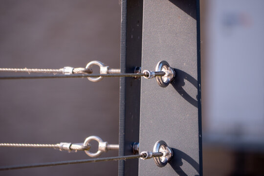 Close-up of stainless steel cable railing attached to a metal post. Modern architectural detail of a wire balustrade system used for safety, support and contemporary design.
