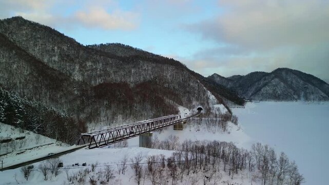 Cinematic approach to the deteriorating Taushubetsu River Bridge standing on frozen lake ice.