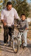 Obraz premium Hispanic father with a prosthetic arm helping his son ride a bicycle on a gravel path, candid and warm moments for family and inclusion themes