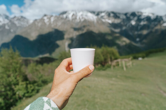 Person holding a light pink cup against a breathtaking panoramic view of the Mountains 