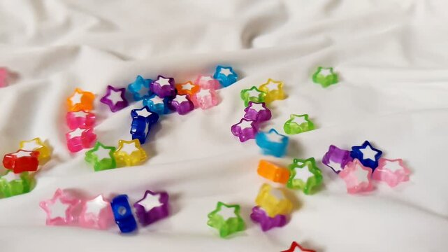 Colorful Star Beads Falling on White Stretch Fabric in Slow Motion