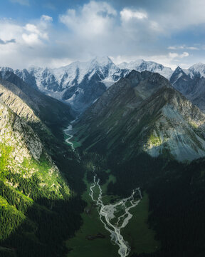 Aerial view of Boris Yeltsin Peak rising above the lush green valley and winding river in Jety-Oguz, Issyk-Kul Region, Kyrgyzstan.