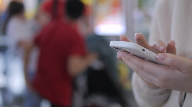 Close-up of hands holding a smartphone. Background shows blurred people moving. Focus on device use in public spaces. Suitable for tech, communication, or urban lifestyle themes