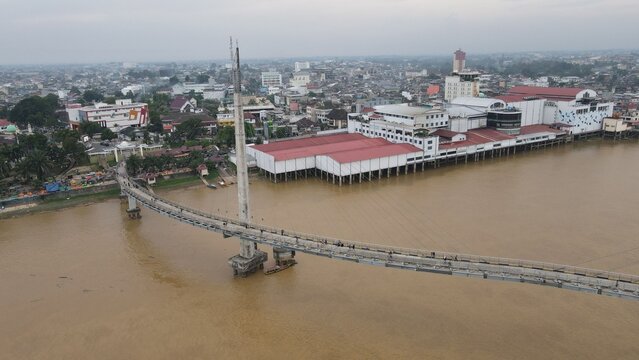 Aerial view of Jembatan Gentala Arasy spanning the Batang Hari River with urban buildings along the waterfront in Kecamatan Jambi Timur, Jambi, Indonesia.