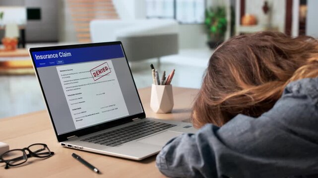 Worried Woman Reads Medical Bill On Laptop At Kitchen Table