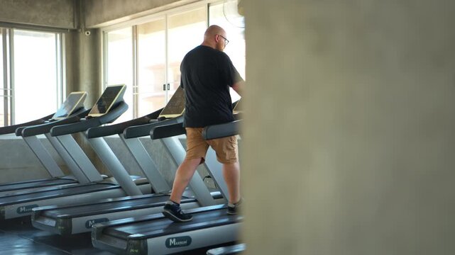 Overweight man walking on a treadmill during a cardio workout and weight loss program in a modern gym