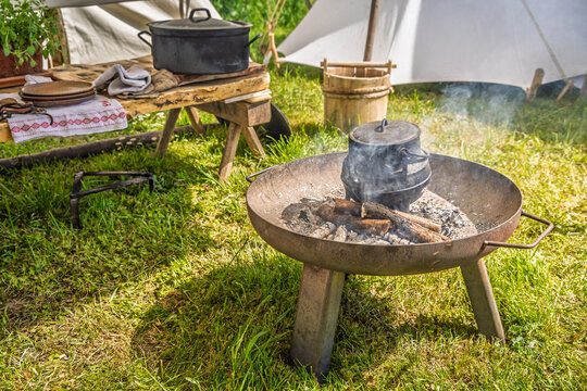 Outdoor cooking with cast iron pot over campfire in a historical reenactment setting