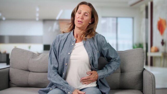 Woman Sitting In Living Room Holding Right Side Feeling Liver