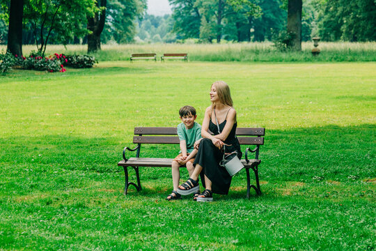Mother with little son on park bench, green shade, summer, travel Europe