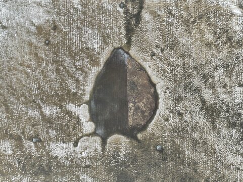 Aerial view of a weathered concrete surface with a central irregular hole revealing dark underlying material in Italy.