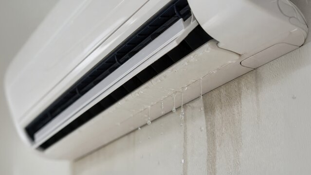 A wall-mounted air conditioner is leaking water, causing visible damage and wet streaks on the wall below it.