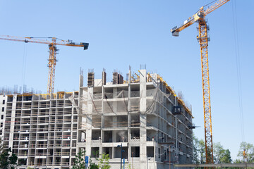 A dynamic view of modern urban construction on a bright, sunny day. Two yellow tower cranes dominate the scene as they build the concrete framework of a large new commercial or residential building © MFV