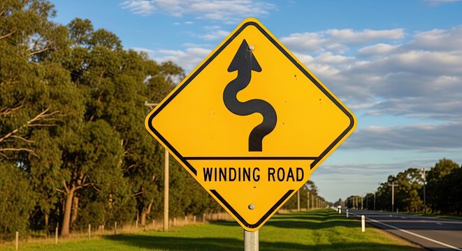 A yellow winding road sign stands prominently against a bright blue sky. The sign features a black, curved arrow indicating a winding road ahead.