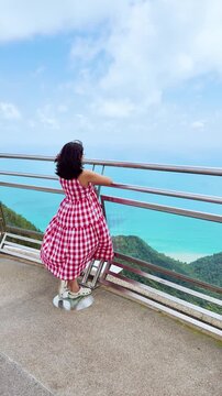 4K Vertical view of Indian woman standing at Langkawi Sky Bridge and looking at view from top at Langkawi, Malaysia. Tourist on Langkawi skycab ride. Girl looking at green hills and blue ocean. 