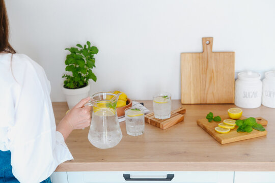 Glass pitcher with lemonade and sliced lemons on a kitchen counter