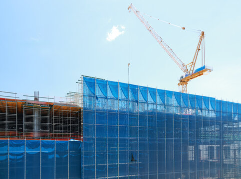 Construction building crane scaffolding blue safety urban architecture development site. Construction site with blue safety netting scaffolding and large crane clear sky showcasing urban