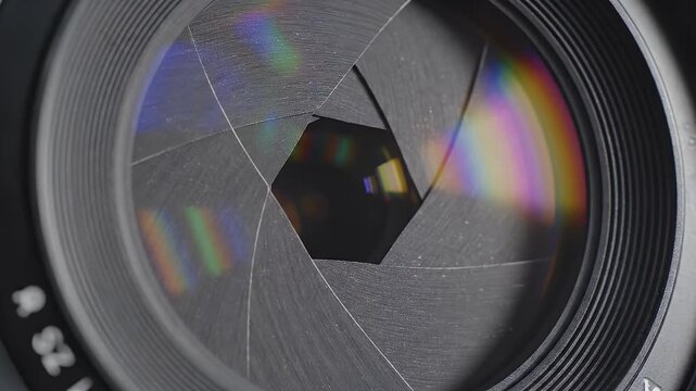 Close-up of a camera lens aperture opening and closing with colorful light reflections.
