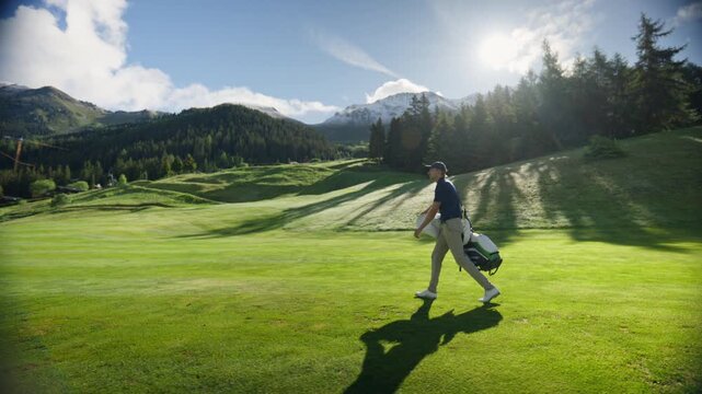 Golfer walking across a pristine alpine golf course carrying a golf bag. Scenic mountain setting, pine forests and dramatic clouds create a premium golf lifestyle atmosphere in Verbier, Switzerland.