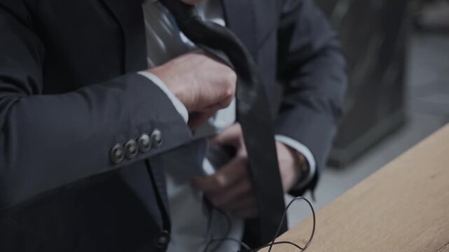 Person puts the microphone through his shirt and attaches it to his jacket. TV presenter or journalist is preparing to go on the air. Man in a business suit is sitting at a table.
