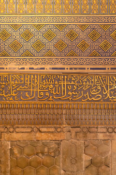 Ornate golden calligraphy and geometric tilework inside Gur-e-Amir mausoleum in Samarkand. Layered bands of Arabic script, painted patterns, and onyx panels showcase Timurid decorative artistry.