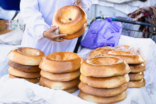 Heap of glossy golden hot round tandoor-baked breads with sesame seeds on vendor stall.  Siab bazaar in sunny day, street food market. Traditional bread naan in asian. Samarkand, Uzbekistan.