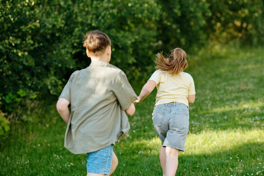 Rear view of children running together through green park