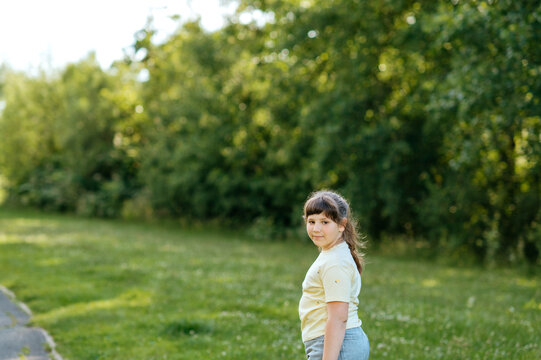 Child girl standing in grassy park with copy space and looking back