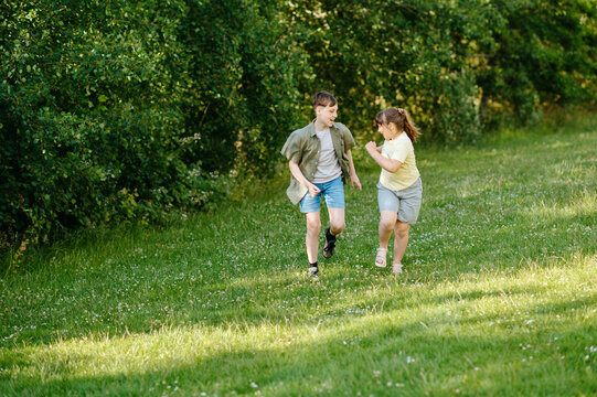 Brother and sister running together across grassy park
