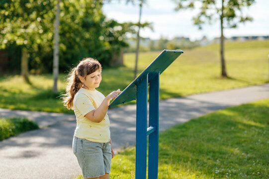 Child girl reading outdoor information sign in local park
