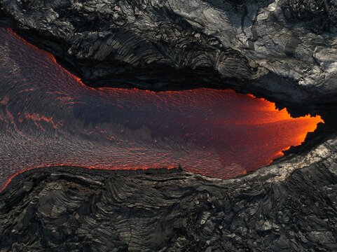 Aerial view of molten lava flowing through a dark volcanic rock channel at the Litli-Hrutur eruption site in Grindavik, Grindavikurbaer, Iceland.