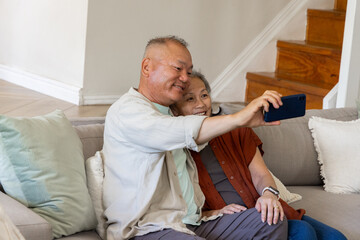 Fototapeta premium Couple sitting close on gray couch in living room, man holding dark-blue smartphone, woman leaning