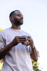 African American man standing in yard holding ceramic cup, wearing light tee, ringed left hand © wavebreak3
