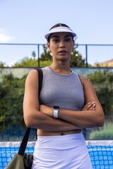 African American woman standing on tennis court by net crossing arms wearing visor smartwatch strap