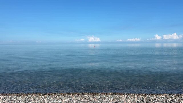 Calm clear blue Black Sea water on a pebble beach under sunny sky in Georgia