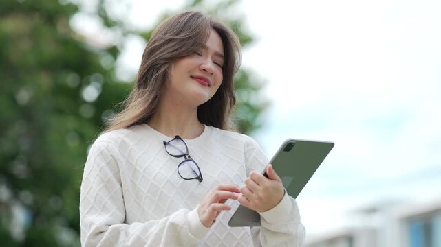 Young female student uses a tablet outdoors on campus, enjoying digital learning and mobile technology.