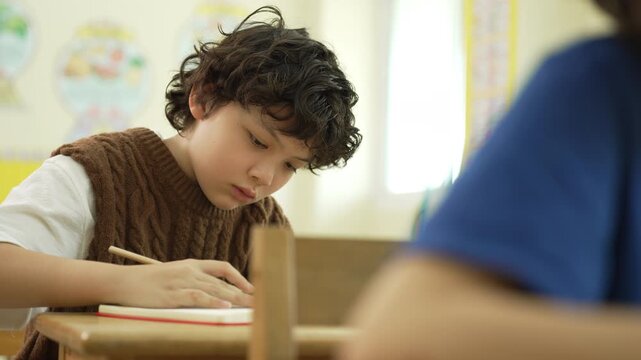 Focused schoolboy writing in a notebook during a classroom lesson, showing concentration and learning.