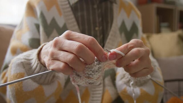 Unrecognizable senior woman knitting with yarn and needles, focusing on hand movements. For retirement home promotions, senior leisure activities, and mental wellbeing