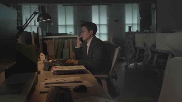 A tired businessman sitting at a classic wooden desk late at night in a dark office glancing away from his computer with a distant look.