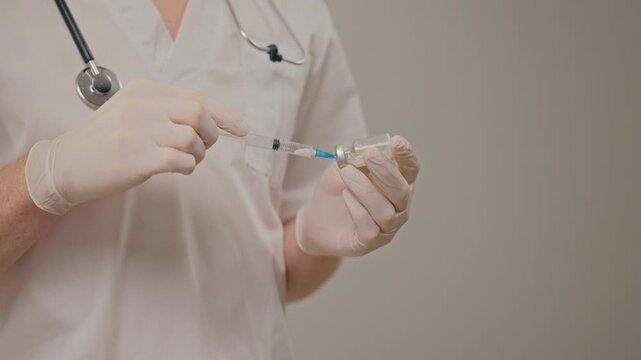 Gloved hands draw vaccine from small vial into syringe, aseptic technique and dose measurement emphasized in focused preparation