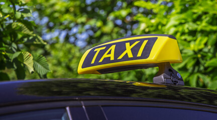 Yellow taxi sign on top of a car with green foliage in the background © Brebca