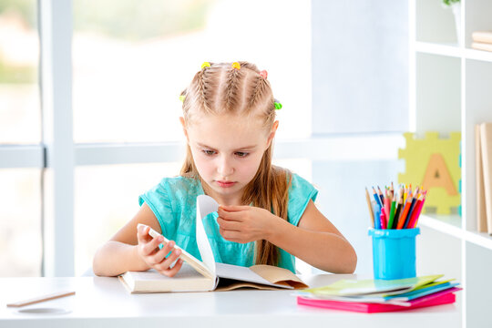 Little Girl Opening A Book While Sitting At A School Desk