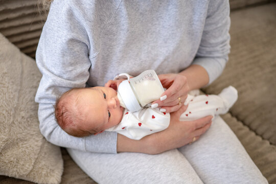 Mother bottle feeds newborn baby wearing white heart print sleepsuit.