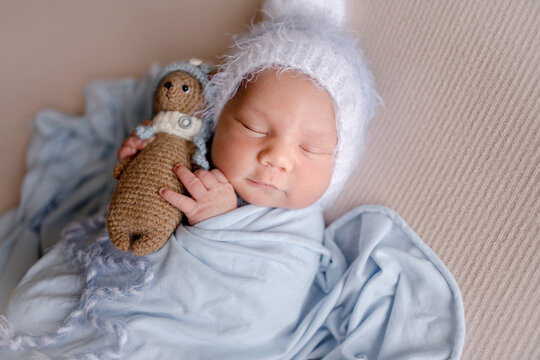 Newborn baby rests peacefully. Baby wears white hat, holds crochet doll. Professional newborn photoshoot.