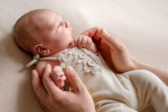 Adult hands gently hold newborn baby lying on soft ribbed blanket. Baby gazes upward.