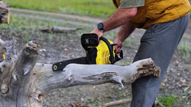 Hands of a middle-aged man showcases his skill with a chainsaw, efficiently cutting a fallen tree. His efforts contribute to a safer outdoor space for everyone to enjoy. Slow motion 4K footage.