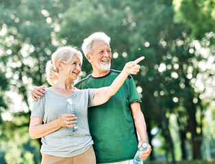 Naklejka premium Smiling active senior couple holding water bottles, drinking and jogging together in the park