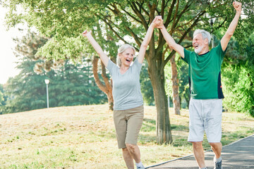 Obraz premium Smiling active senior couple jogging exercising and having fun and celebrating success rasing hands together taking a break in the park