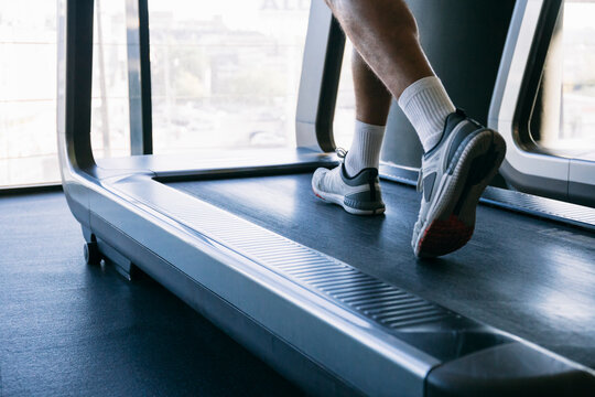 Legs of male athlete running on treadmill in gym