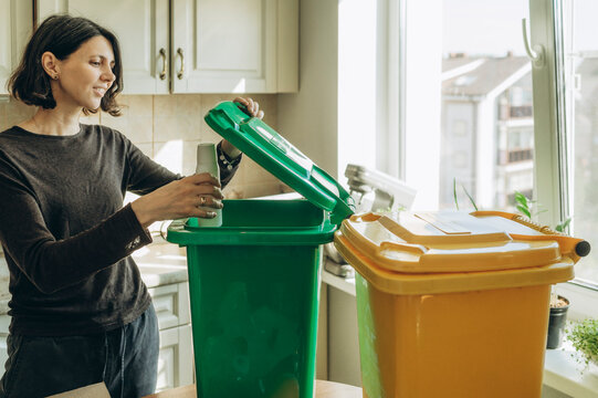 Woman sorting plastic bottle into green recycling bin at home